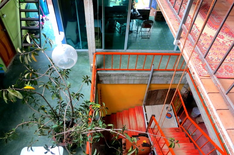 Looking down an open stairwell inside the earthen house, orange stairs against teal floors