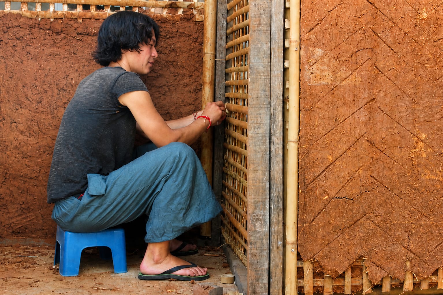 A student smiles in profile while weaving a bamboo lattice panel into an earthen wall