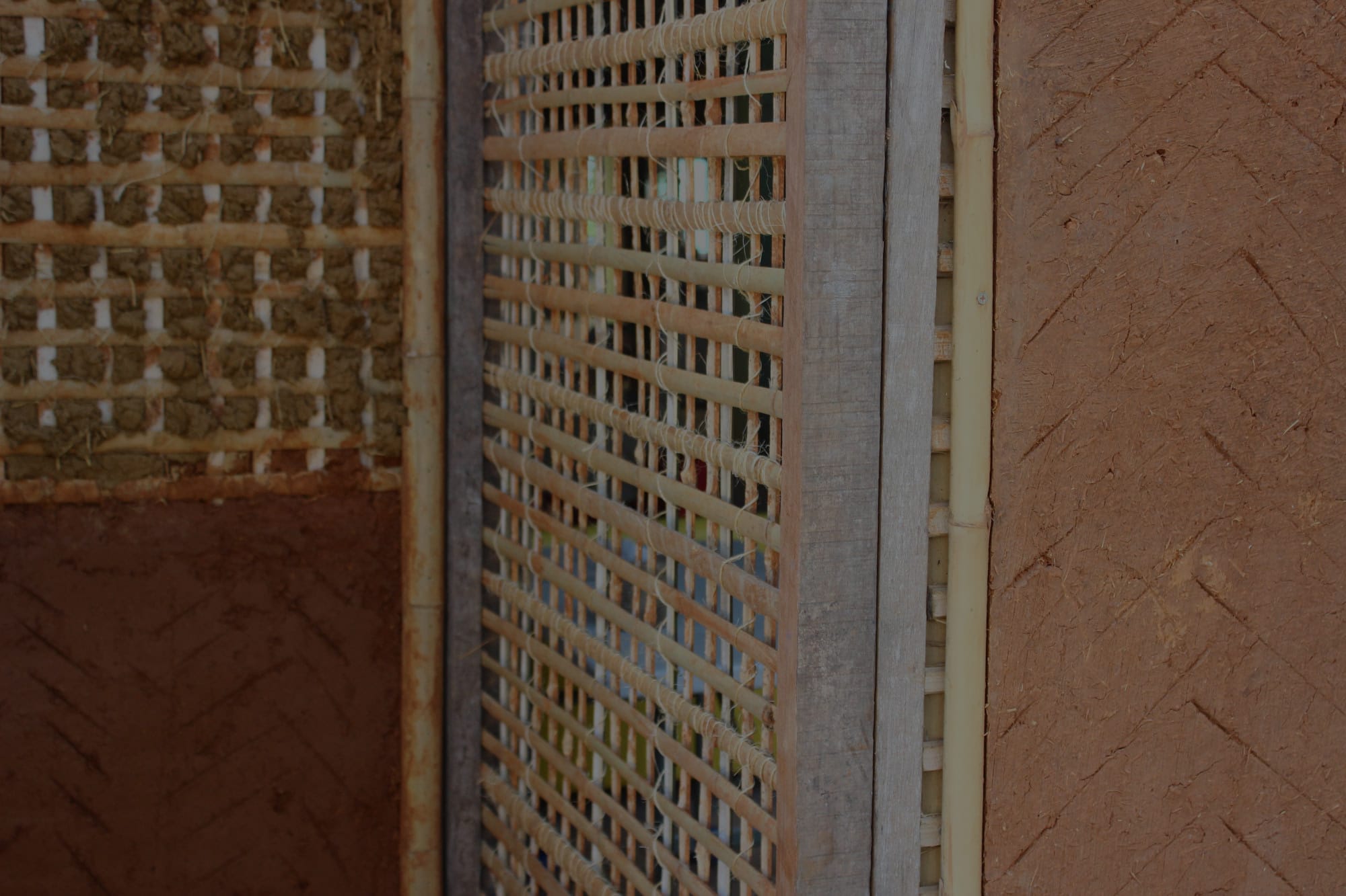 Detail of a natural building wall under construction, woven bamboo lattice beside layered red-oxide earthen plaster