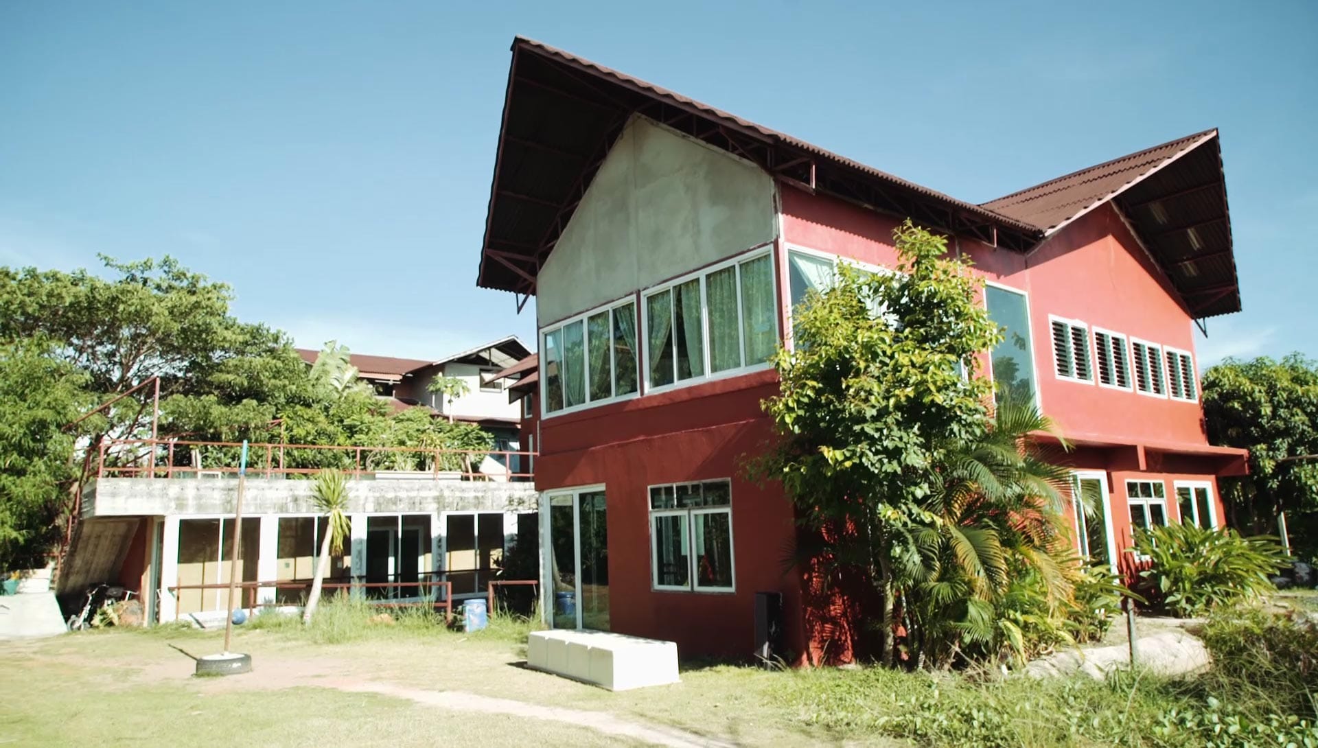 Wide exterior view of a two-storey red and cream farm building with steep gabled roofs and ground-floor glazed sections