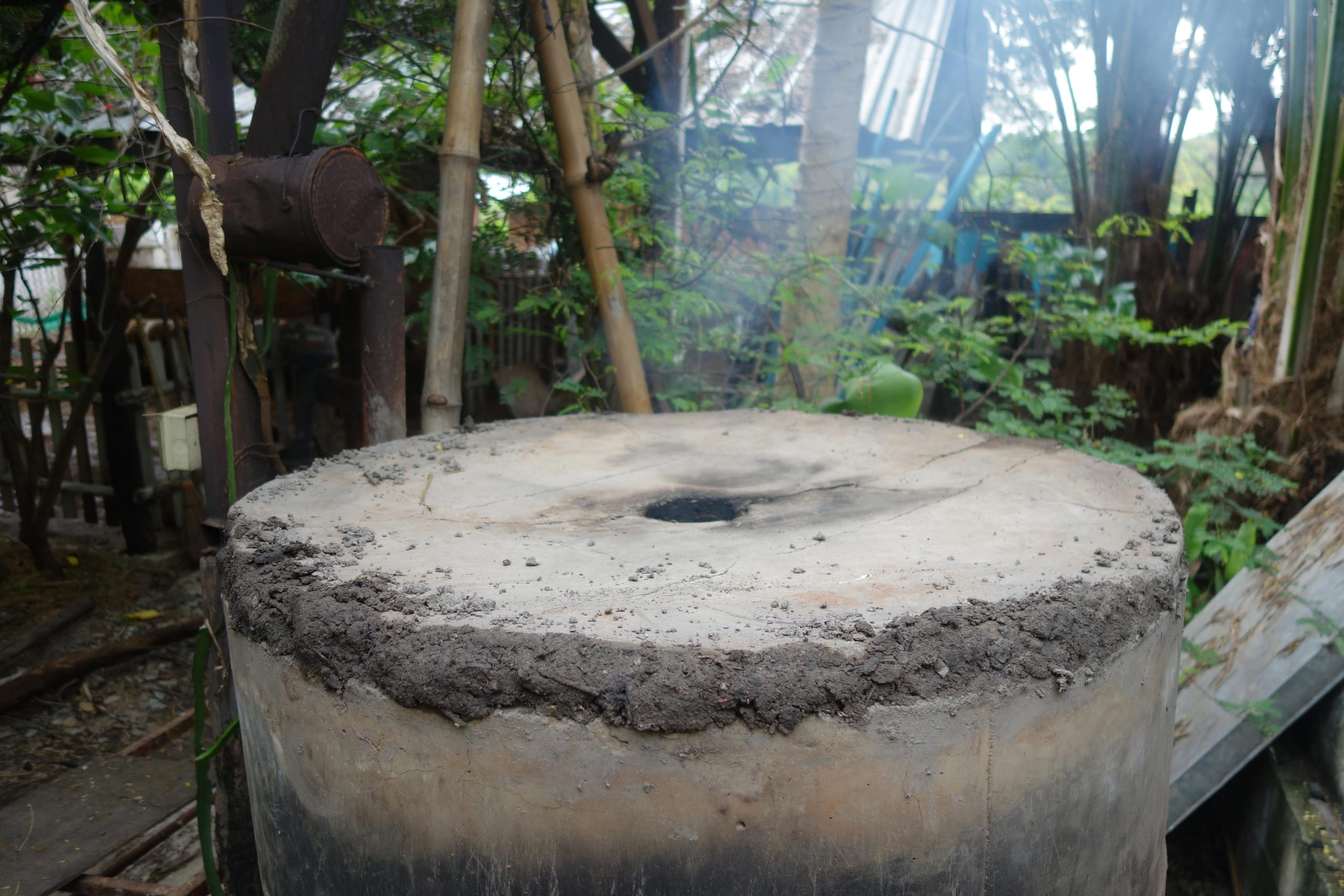 A biochar kiln mid-burn, its concrete lid venting smoke through a central hole
