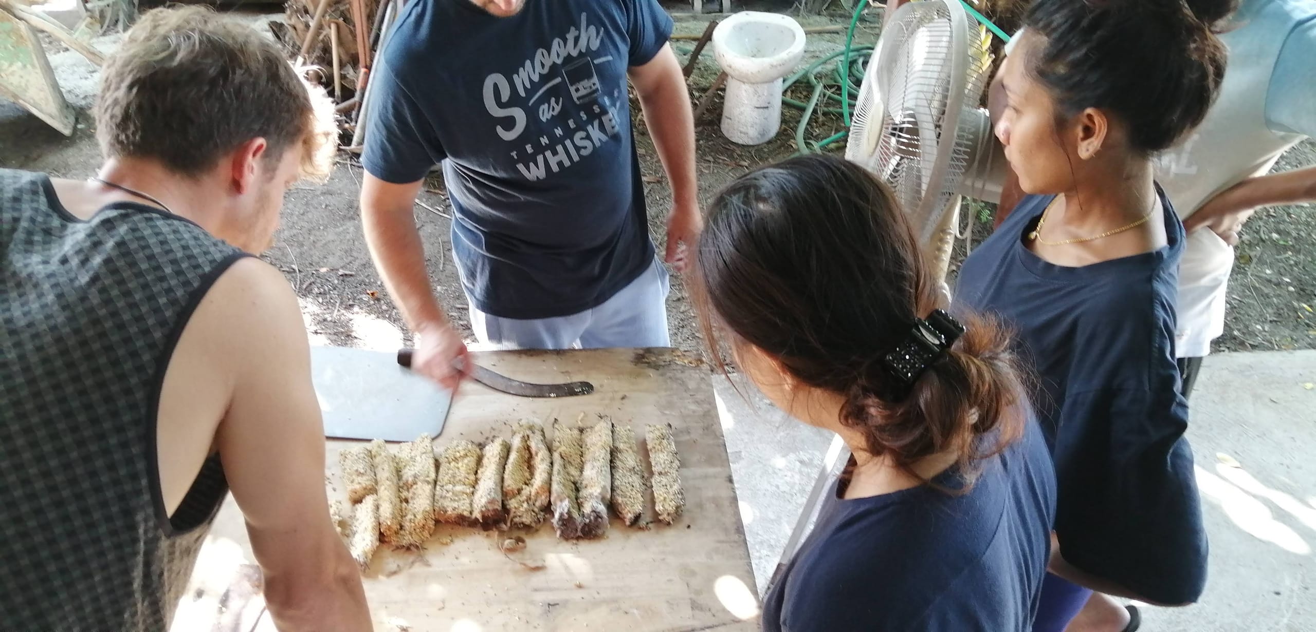 Four students and an instructor gathered around a table during a natural building class, watching an earthen sample stick being cut