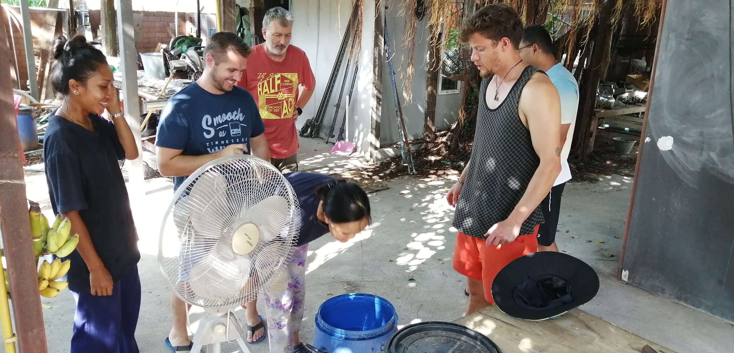 A course group mixing a batch of natural plaster outdoors under a shelter