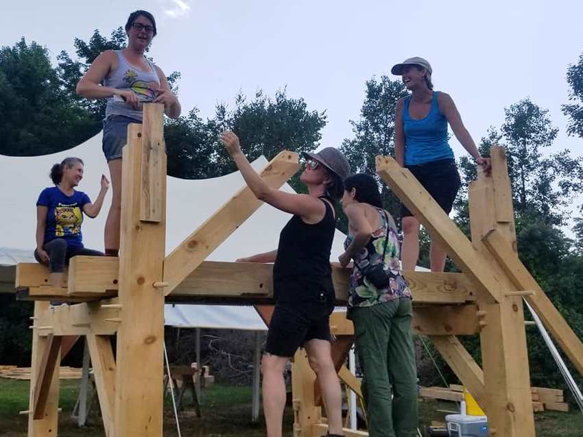 Five women laughing together on a timber frame at dusk during a natural building session at Daruma