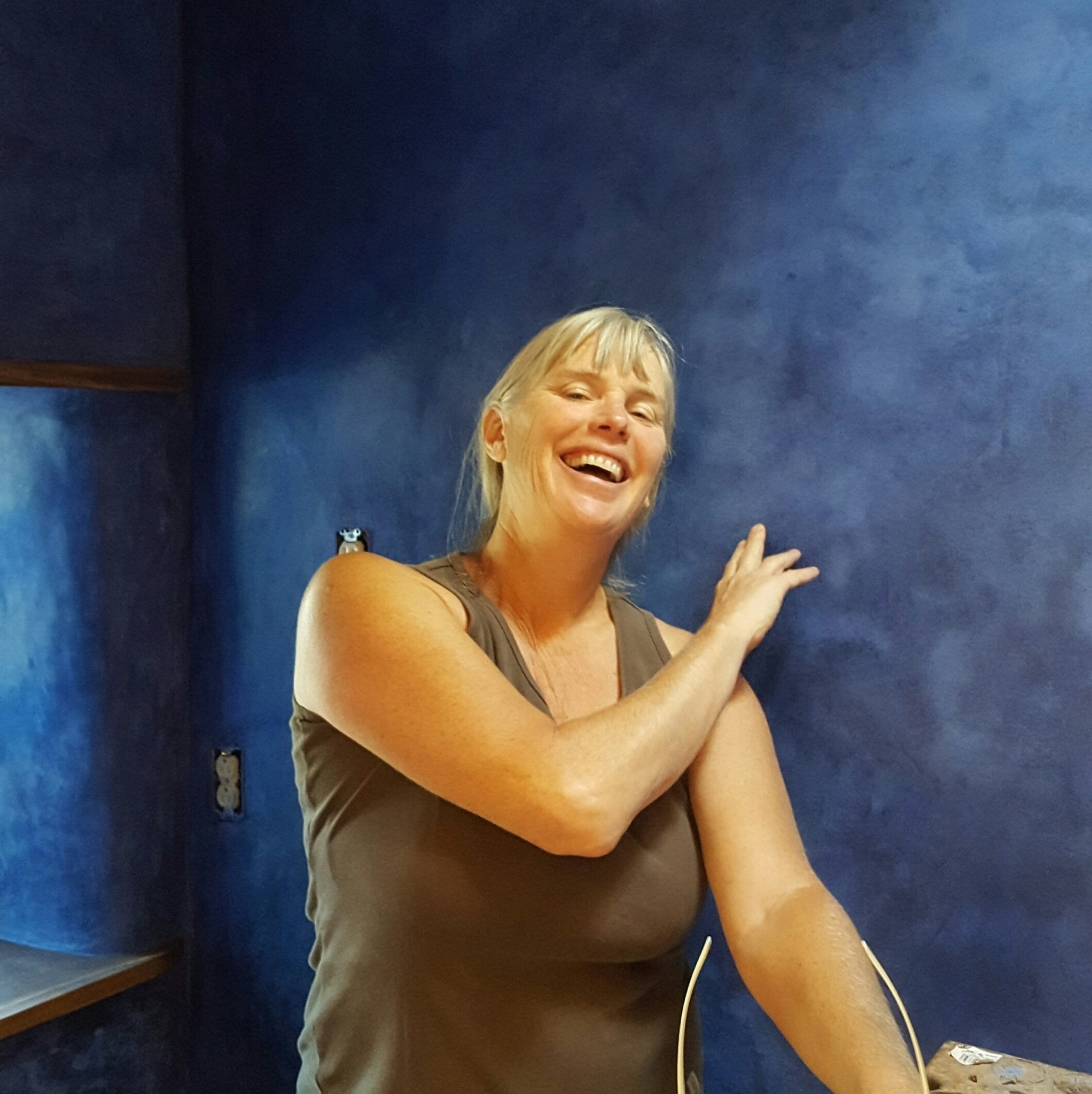 A volunteer smiling in front of a freshly finished blue plaster wall