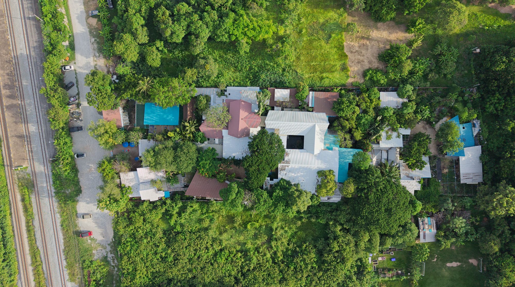 Drone view of the Mosaic School campus with a pool and gravel road running alongside the railway line