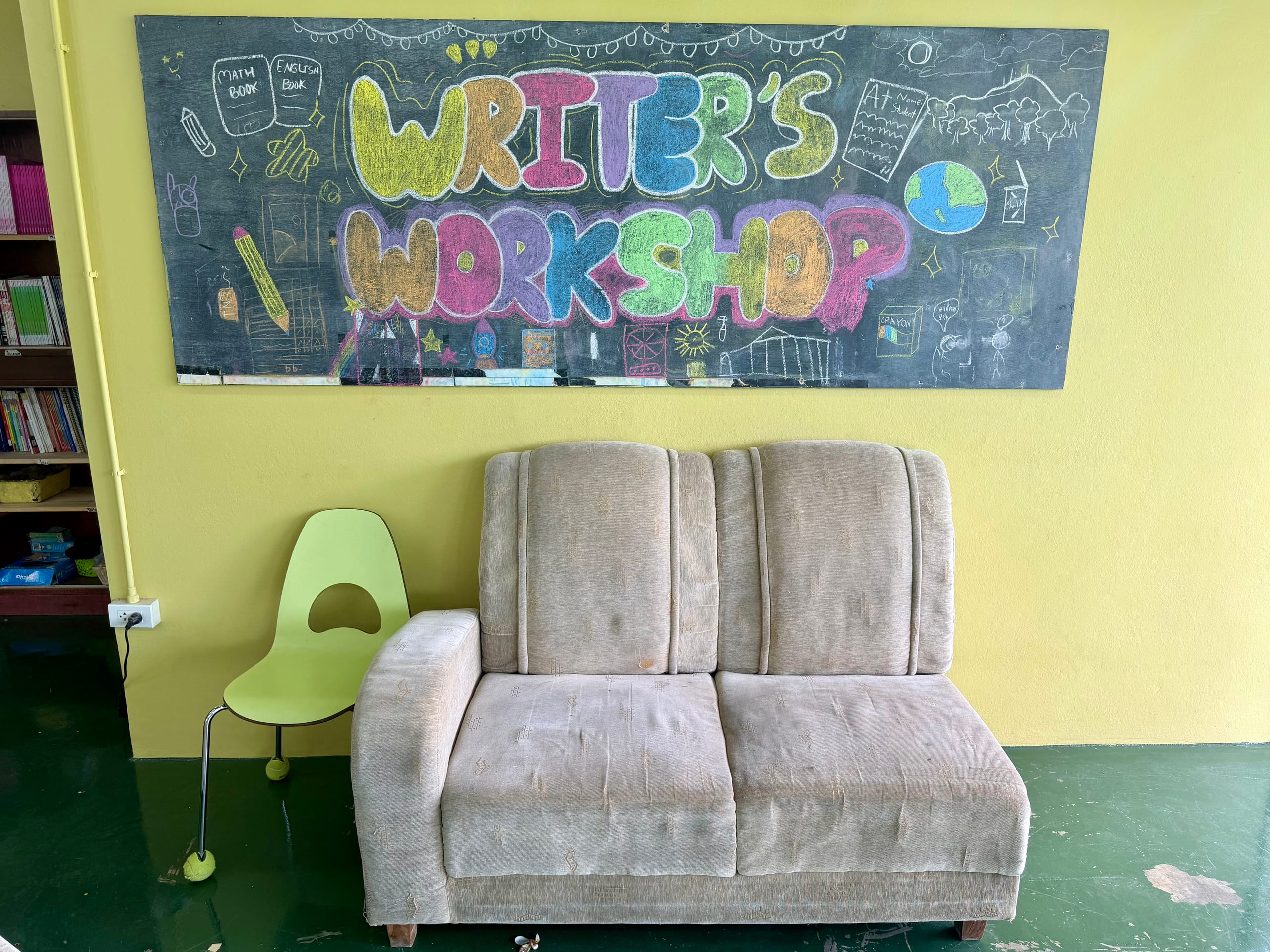 Hand-lettered Writer's Workshop chalkboard sign in a Mosaic School classroom, above a reading corner
