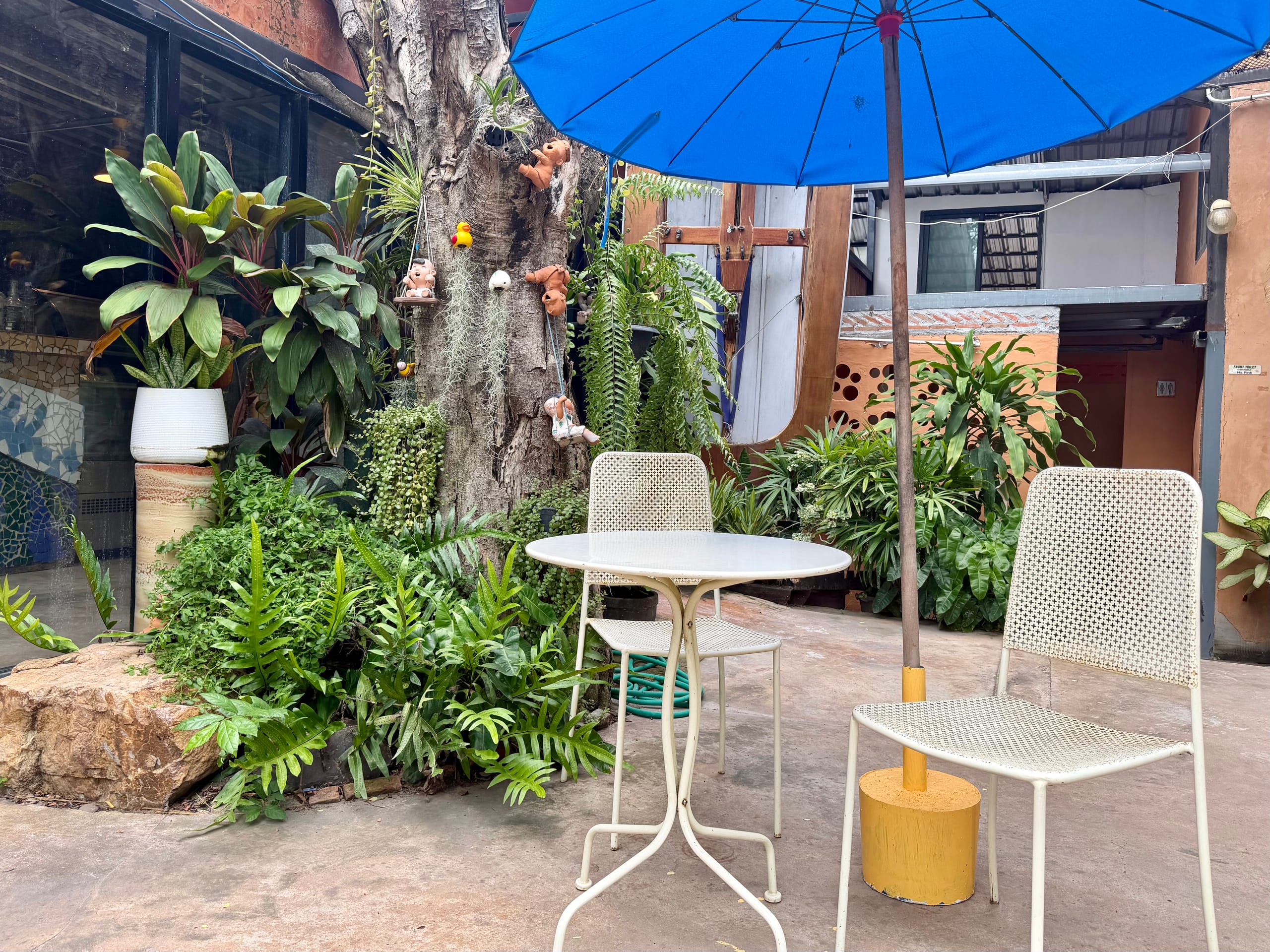 A shaded courtyard seating area with table and umbrella beside a planted wall at Mosaic School
