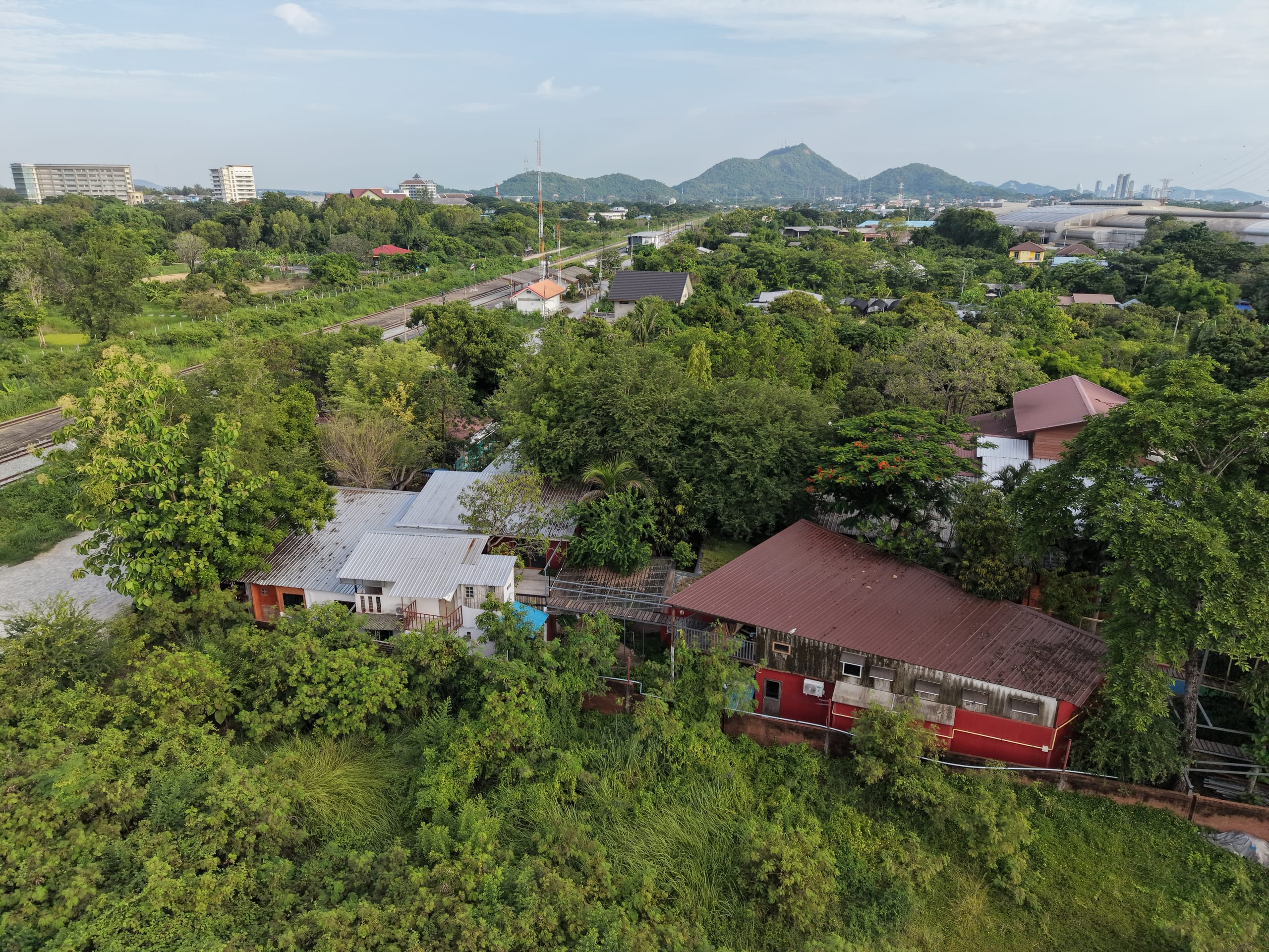 Aerial view of a red-roofed building beside the railway line, with a distinctive pointed hill on the horizon near Bang Phra