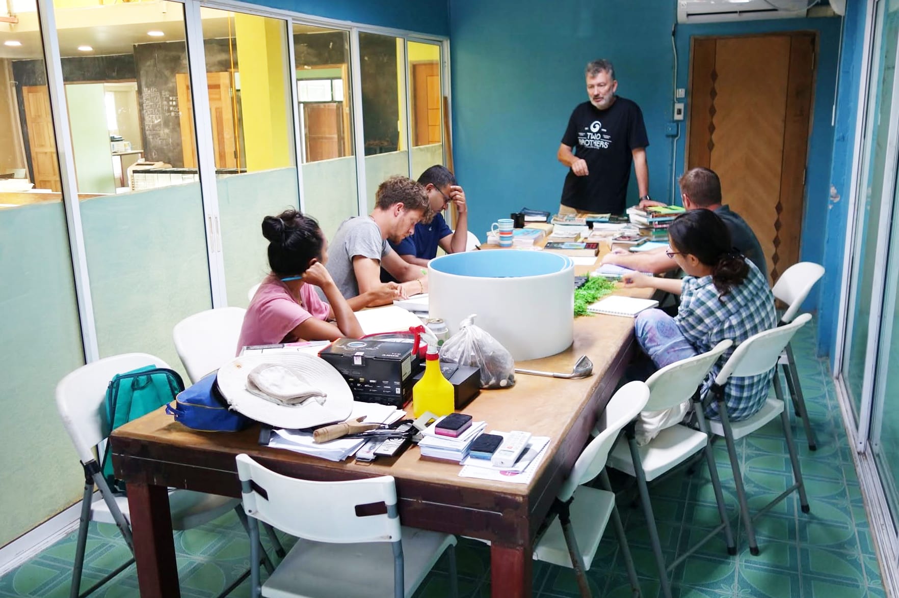 A group gathered around a cluttered workshop table indoors for a planning session