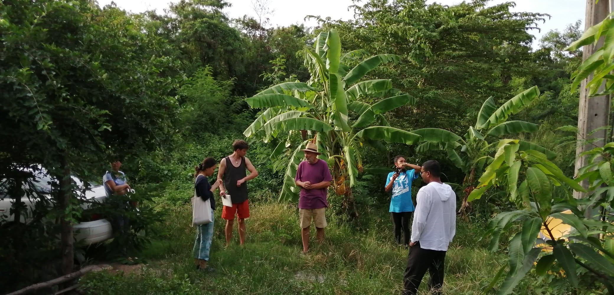 Six course participants standing together in a grassy clearing ringed by banana plants and forest