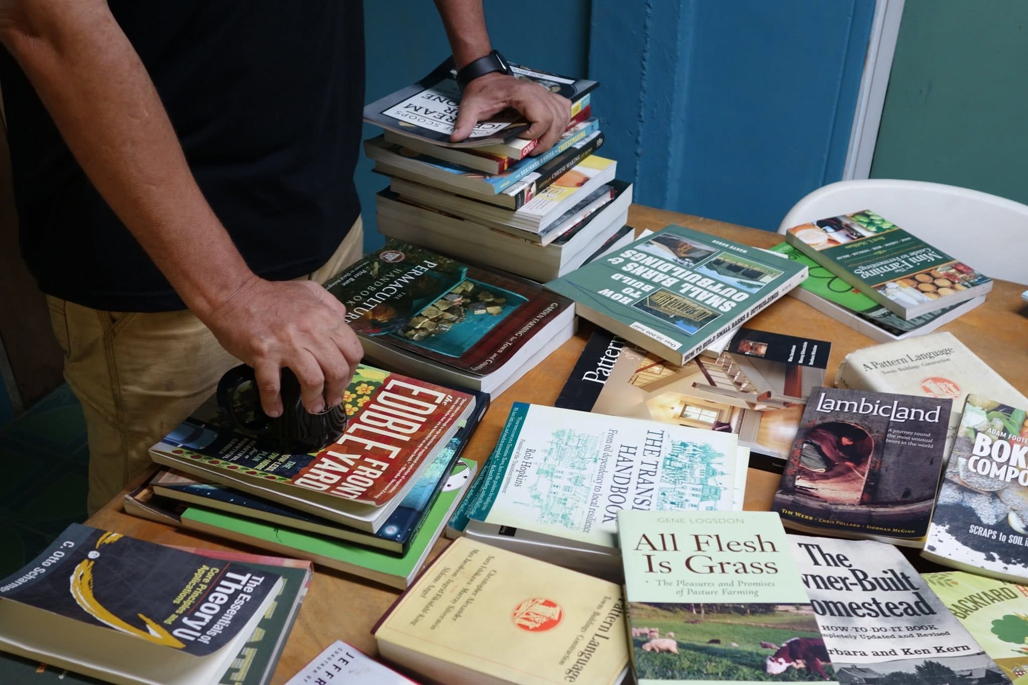 Hands stacking a pile of permaculture and homesteading books on a table