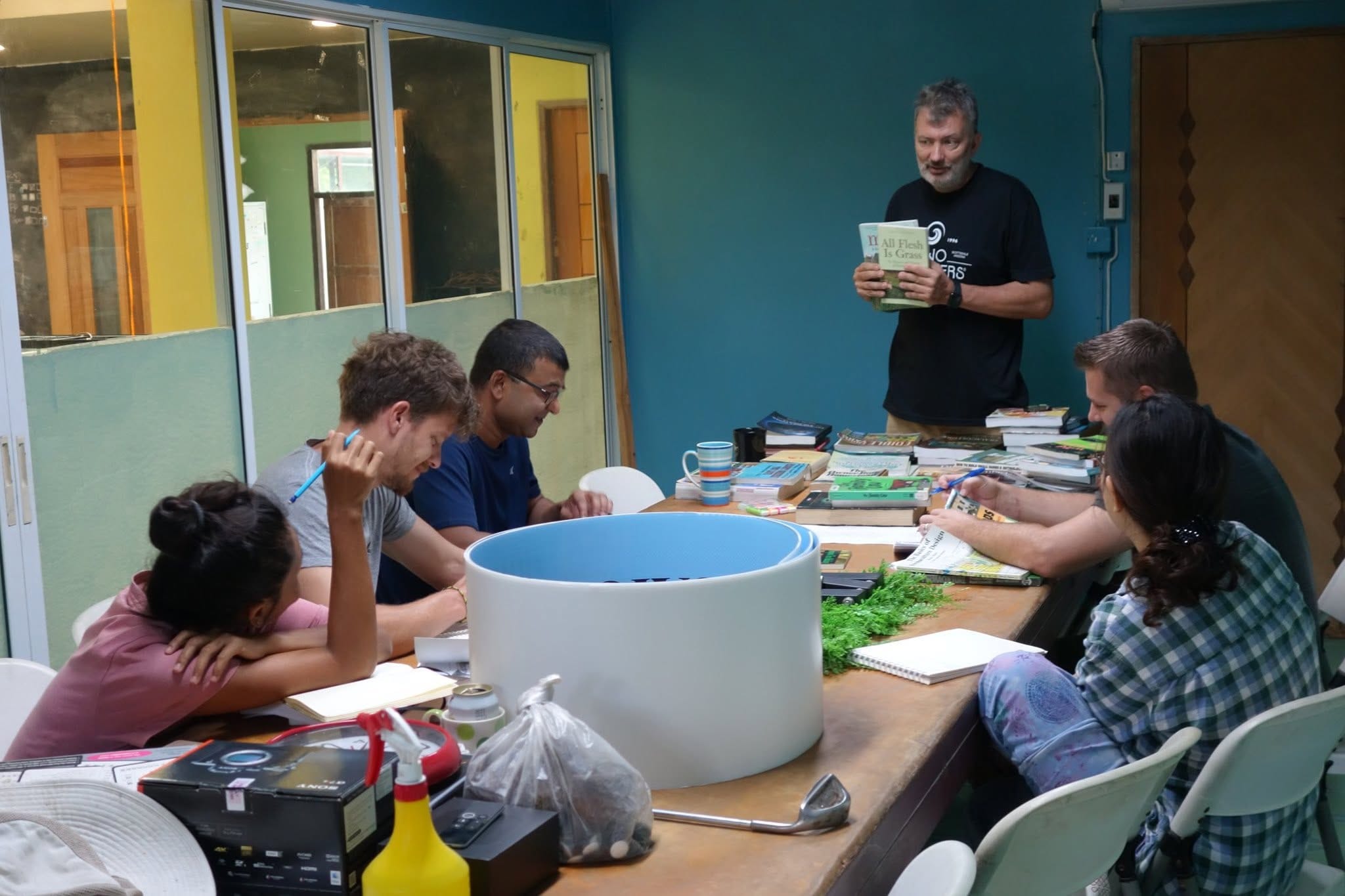 An instructor holding up All Flesh Is Grass while students look through stacks of books