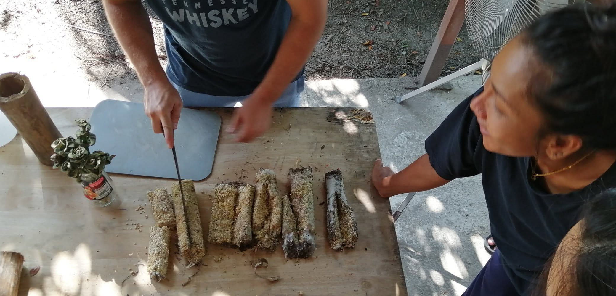 Overhead view of hands cutting and arranging grain-coated mushroom log sections on a wooden table during an Alchemy course demonstration