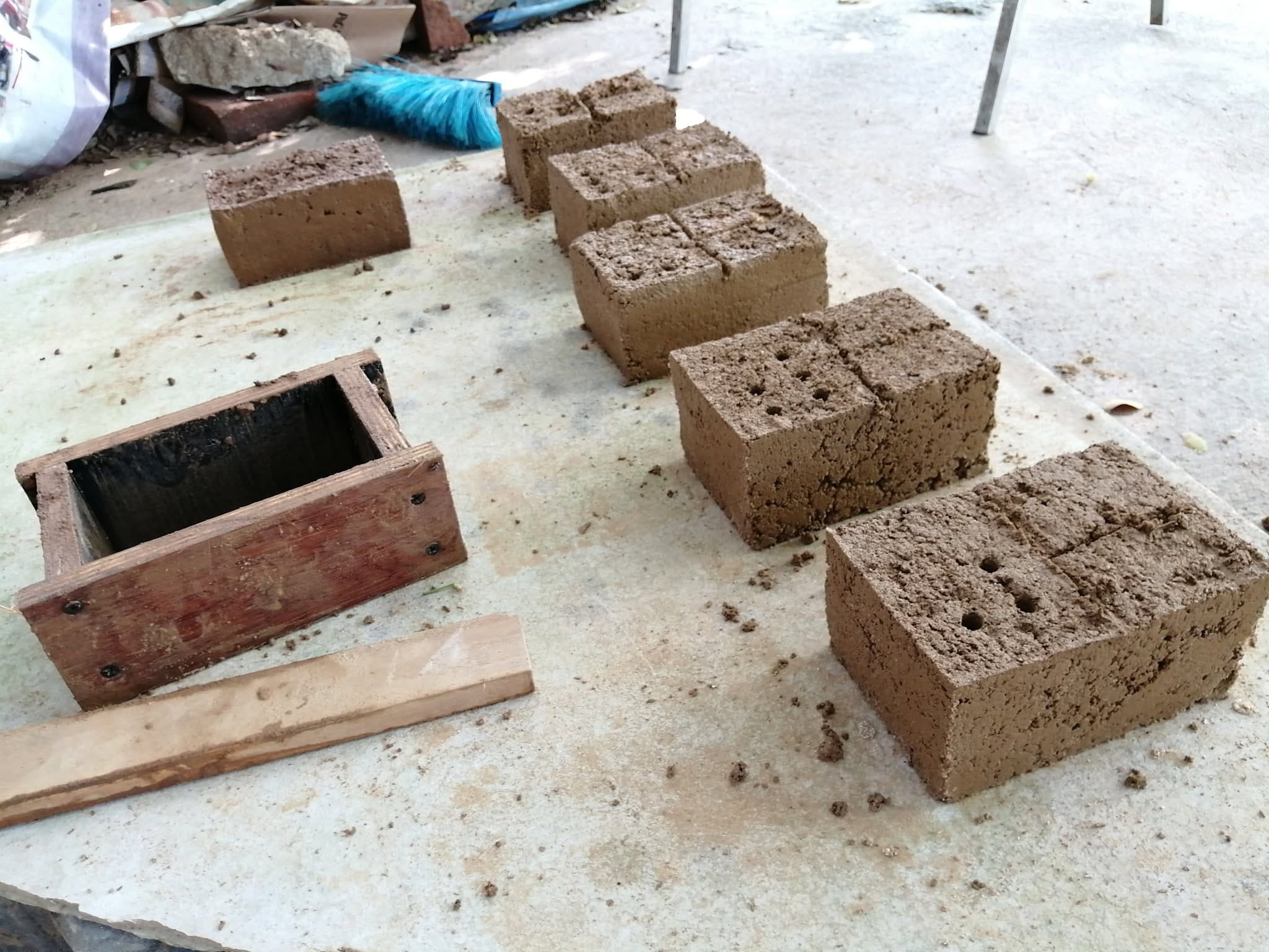 Six finished earthen bricks drying on a concrete surface at Daruma