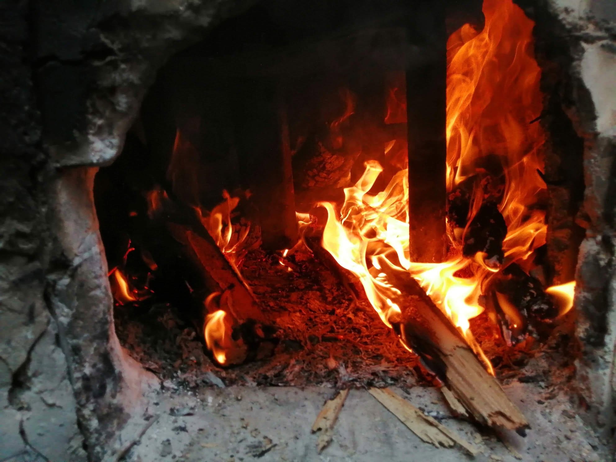 Close view into a wood-fired kiln, bright orange flames and embers over a bed of ash