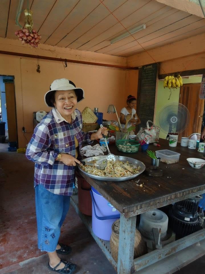 A smiling cook in a sun hat stirring noodles in a pan at Daruma's outdoor kitchen